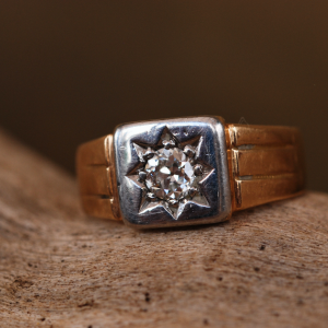 A photograph of an Edwardian 18ct yellow gold diamond signet ring on top of driftwood.