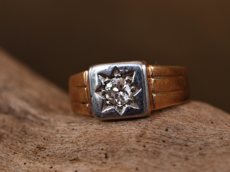 A photograph of an Edwardian 18ct yellow gold diamond signet ring on top of driftwood.