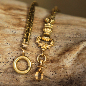 A photograph of an 18k Georgian fist pendant and chain displayed over a piece of driftwood.