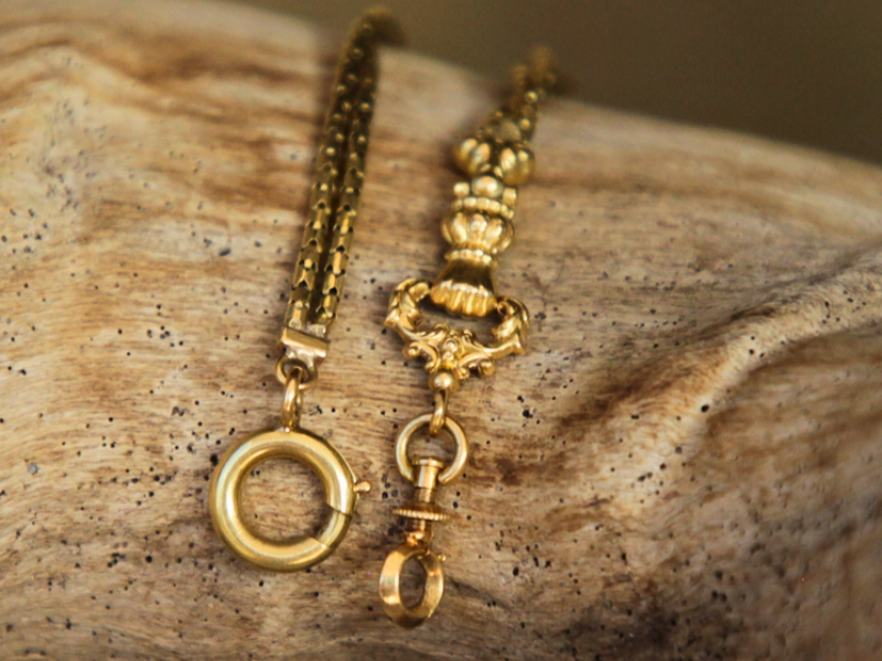 A photograph of an 18k Georgian fist pendant and chain displayed over a piece of driftwood.