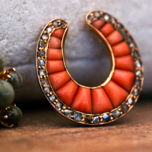 A front-view photograph of a Victorian gold and coral old-cut diamond pendant propped up against a grey rock.