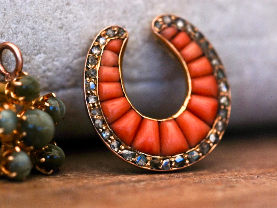 A front-view photograph of a Victorian gold and coral old-cut diamond pendant propped up against a grey rock.