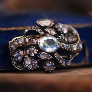 An image of the front of a Georgian aquamarine and diamond brooch propped against a royal blue and gold box.