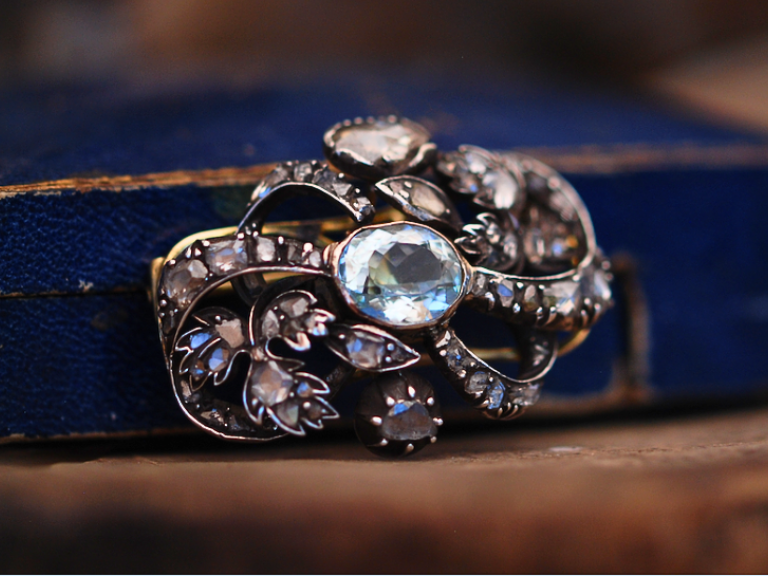 An image of the front of a Georgian aquamarine and diamond brooch propped against a royal blue and gold box.