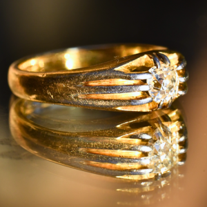 A side-view photograph of a gold Victorian diamond belcher ring and it's reflection on a glass surface.