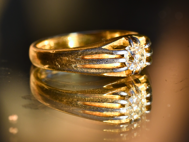 A side-view photograph of a gold Victorian diamond belcher ring and it's reflection on a glass surface.