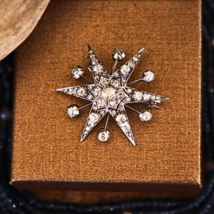 A photograph of a Victorian diamond star brooch and pendant placed on top of a earthy box.