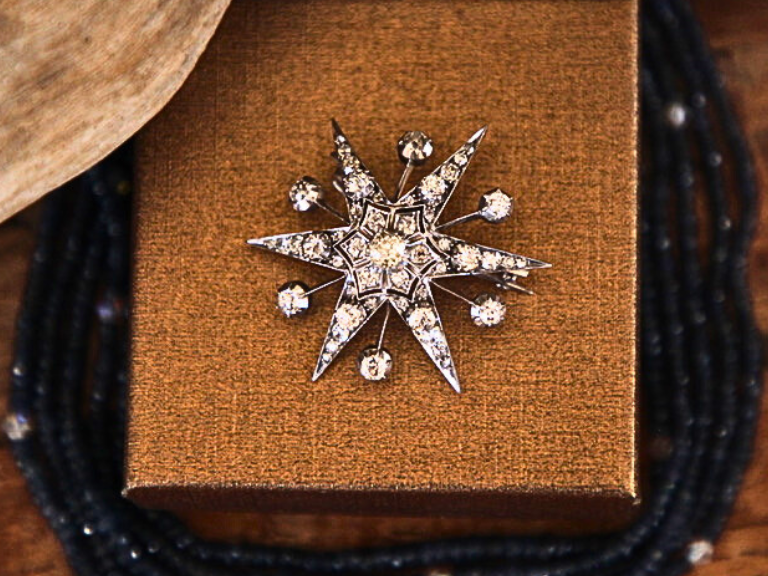 A photograph of a Victorian diamond star brooch and pendant placed on top of a earthy box.
